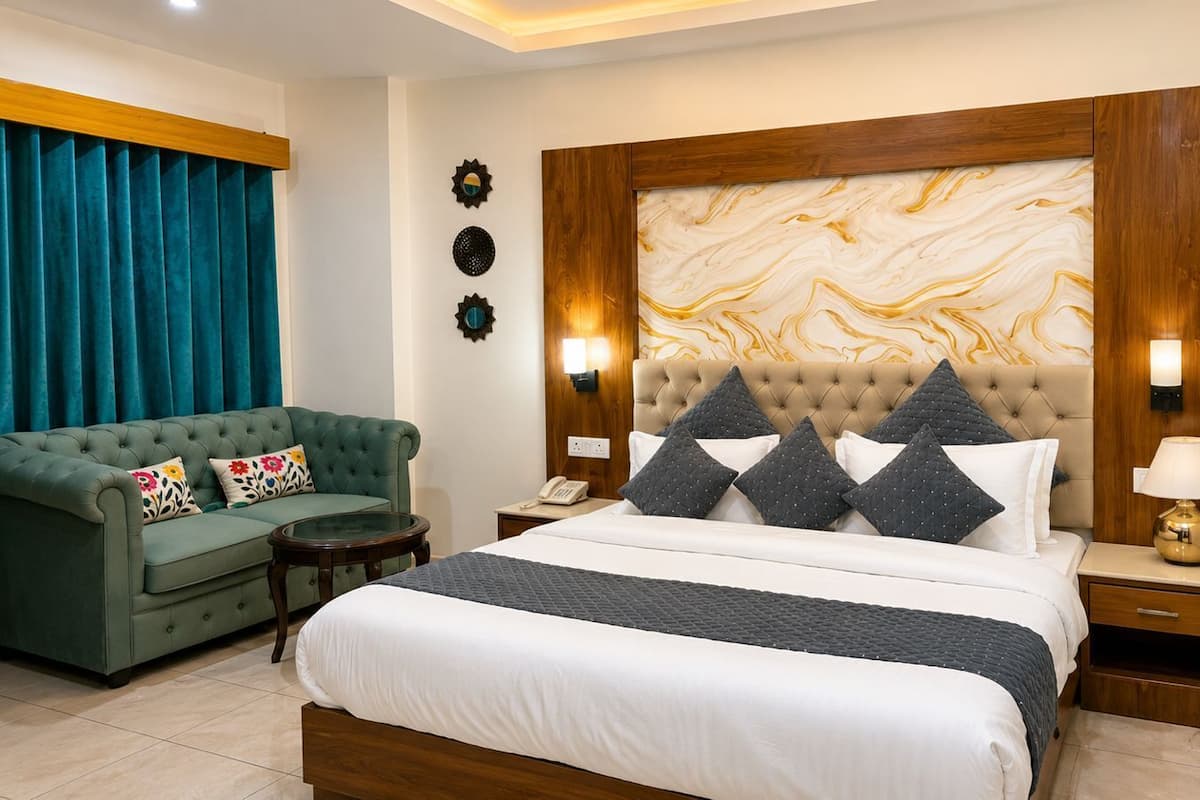 A bedroom with a large bed, a green sofa, a nightstand with a lamp, and a wall-mounted TV.
