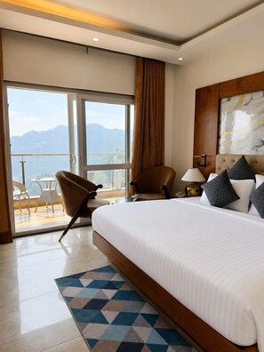 A hotel room with a large bed, a view of mountains, a balcony with chairs, and a modern design. - Hotel Nuri's Mountain Glow (Dehradun)