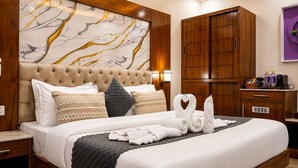 A hotel room with a large bed, wooden headboard, marble artwork, a wardrobe, and a small desk with toiletries.