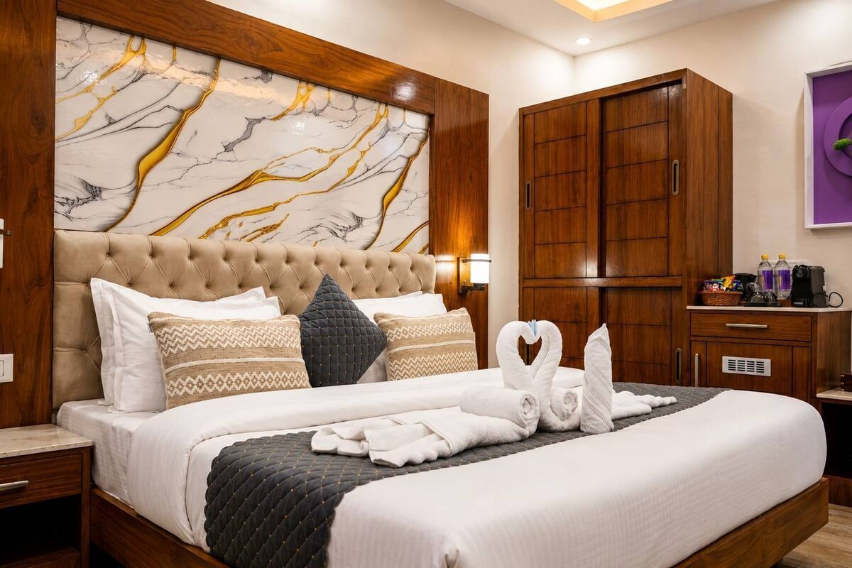 A hotel room with a large bed, wooden headboard, marble artwork, a wardrobe, and a small desk with toiletries.