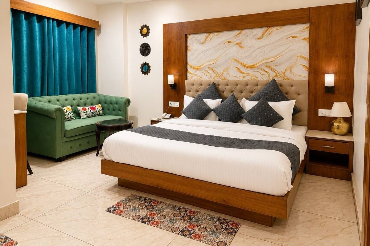 A bedroom with a large bed, a green sofa, a wooden headboard, and a marble-patterned wall.