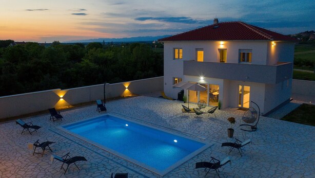 Une maison moderne dotée d’une piscine, d’un espace extérieur aménagé et d’un patio bien éclairé.