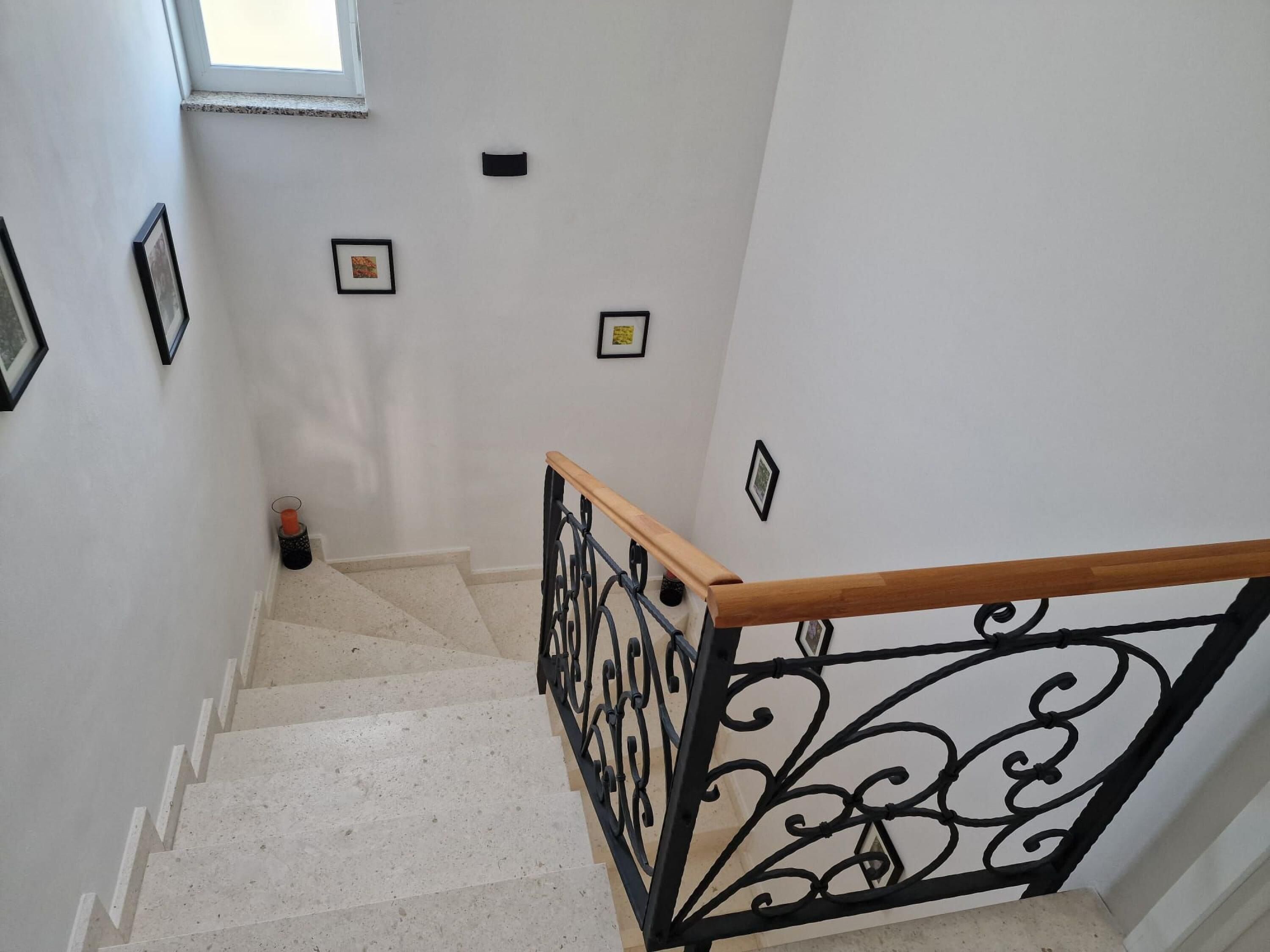 A staircase with a wooden handrail and black metal balusters, leading to a landing with framed pictures on the wall.