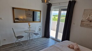 Une chambre d’hôtel avec un lit, une petite table et des chaises, un miroir et une vue sur l’extérieur, accessible par une porte coulissante.