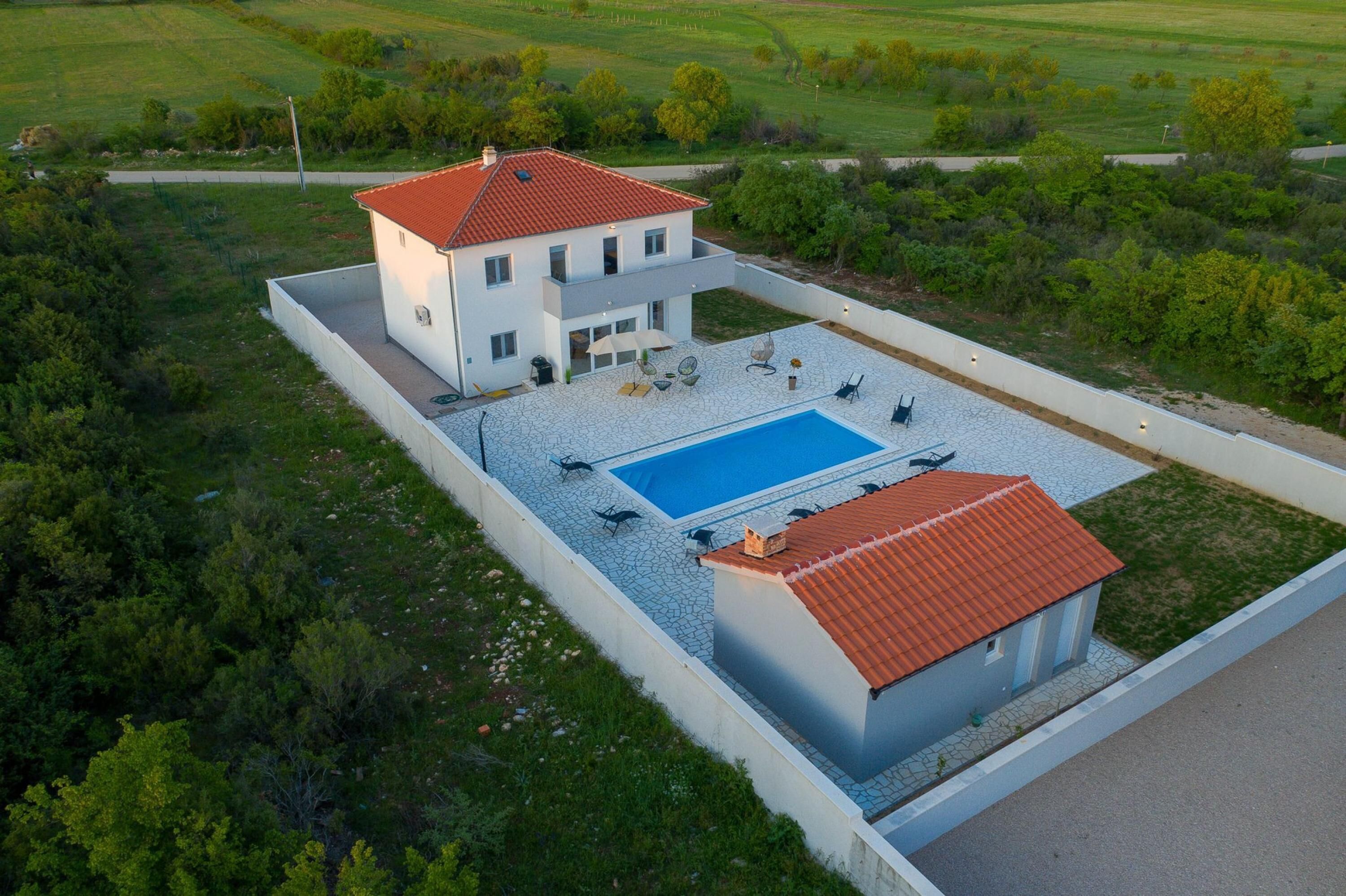 Une maison moderne dotée d’une piscine, entourée d’une zone pavée et de verdure.