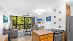 A modern kitchen with a built-in oven and refrigerator, a dining area with a table and chairs, and a large sliding glass door leading to a balcony with a view of palm trees. - Modern Beautiful Renovated Maui Vista 3220 (Kihei)