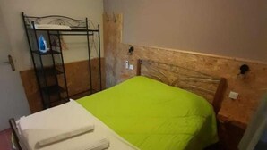 En enkelt seng med grøn og hvid dyne, et træsengegærde og en metalkasse mod væggen.
