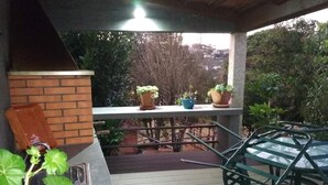 En overdækket terrasse med murstensvæg, metalbord og plantekasser.
