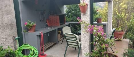 Un patio exterior con una parrilla, sillas y plantas en macetas.