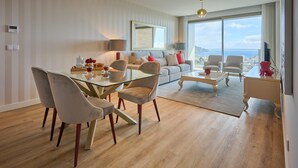 A modern living room with a glass dining table, comfortable seating, a large sofa, and a view of the sea. - Panoramic Pearl by Homie (Funchal)