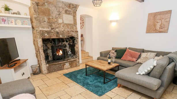 A cozy living room with a stone fireplace, a grey sofa, a coffee table, and a TV on a wooden stand. - The Cottage (Leeds)