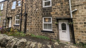 A stone-built terraced house with a white door, a small garden, and a satellite dish. - The Cottage (Leeds)