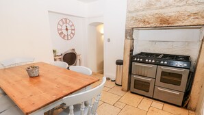 A kitchen with a wooden table, white chairs, a clock, and a stove. - The Cottage (Leeds)