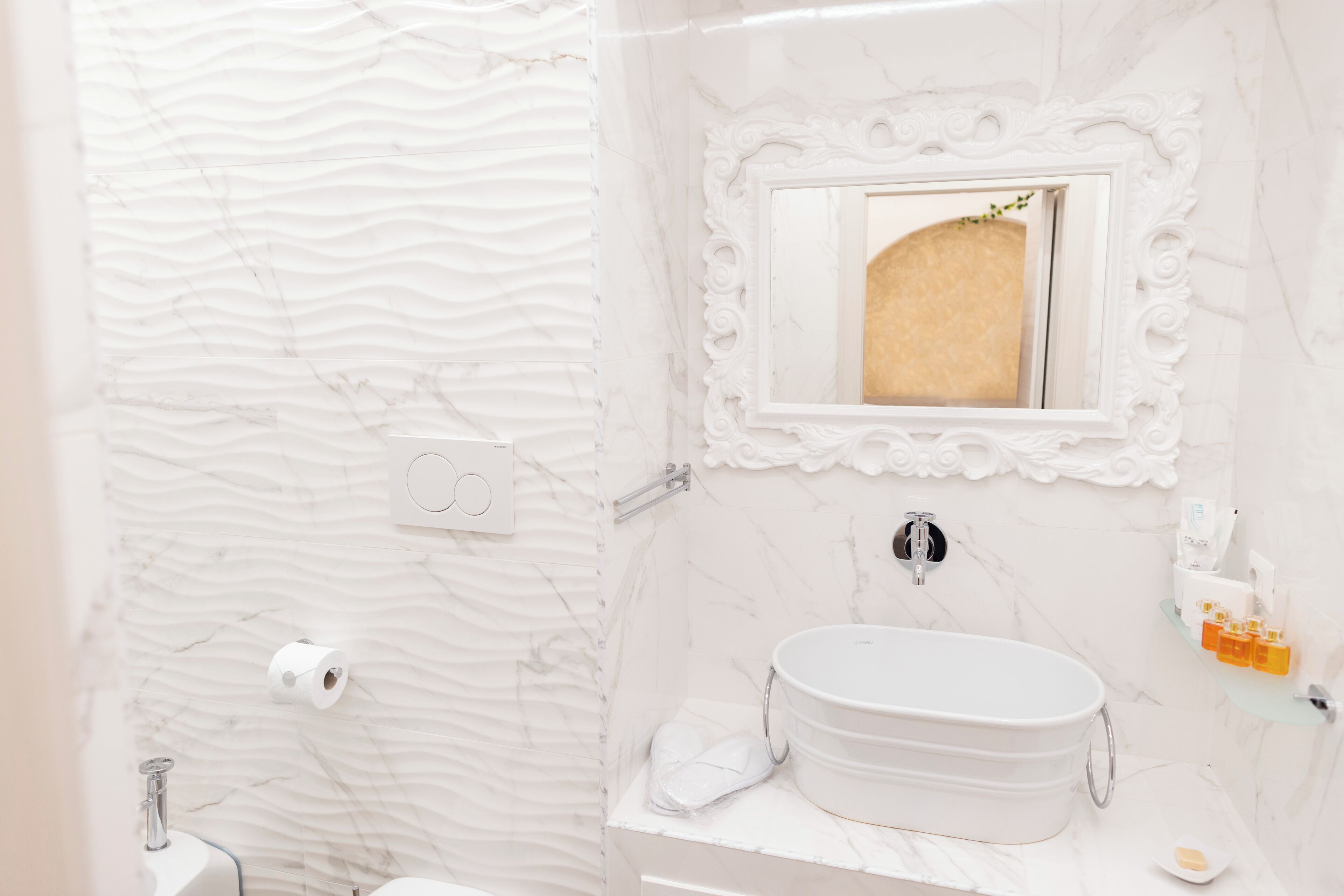 Un baño con pared de mármol, un lavabo con espejo y artículos de aseo en la encimera.