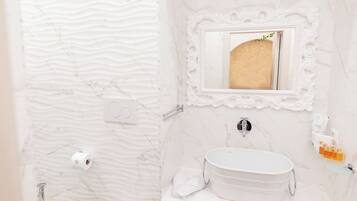 Un baño con pared de mármol, un lavabo con espejo y artículos de aseo en la encimera.