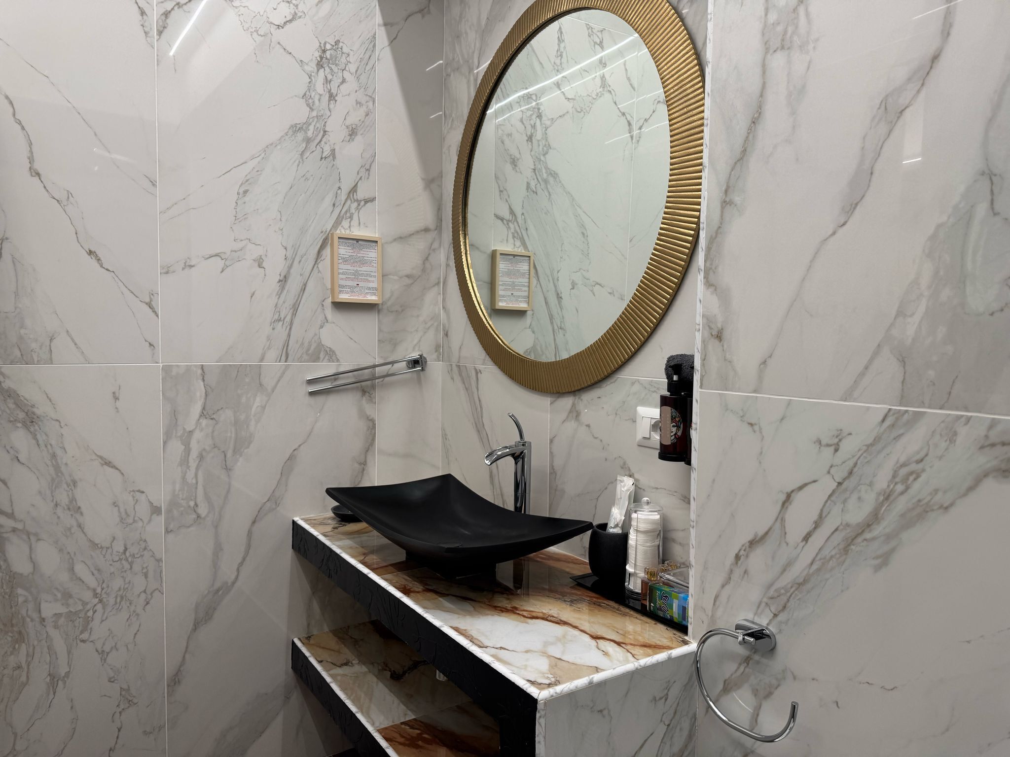 A bathroom with a marble vanity, a gold-framed mirror, a towel rack, and a hand dryer.