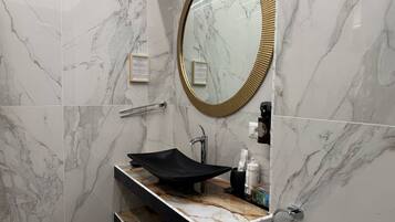 A bathroom with a marble vanity, a gold-framed mirror, a towel rack, and a hand dryer.