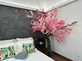 Un dormitorio con cama, almohadas, una mesita de noche, una lámpara y un llamativo arreglo floral rosa artificial.