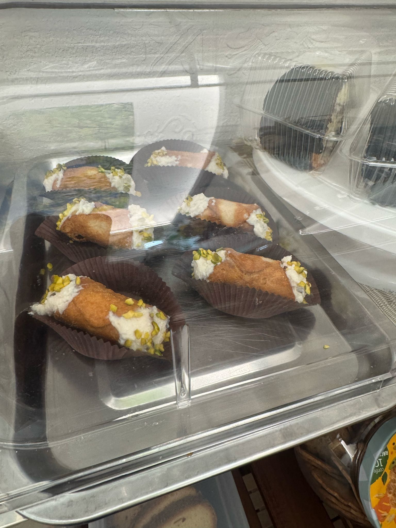 A food display case with pastries in brown paper cups, some with white cream and pistachios.