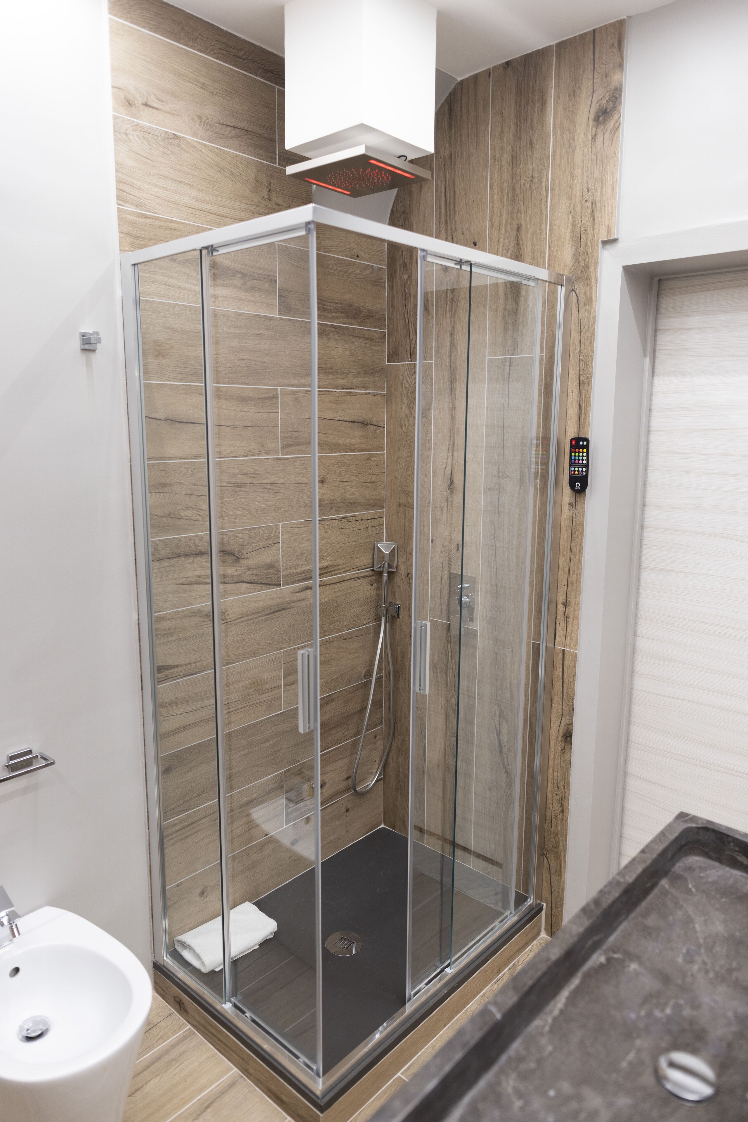 Un baño moderno con ducha envuelta en vidrio, un lavamanos blanco y un panel de pared de madera.