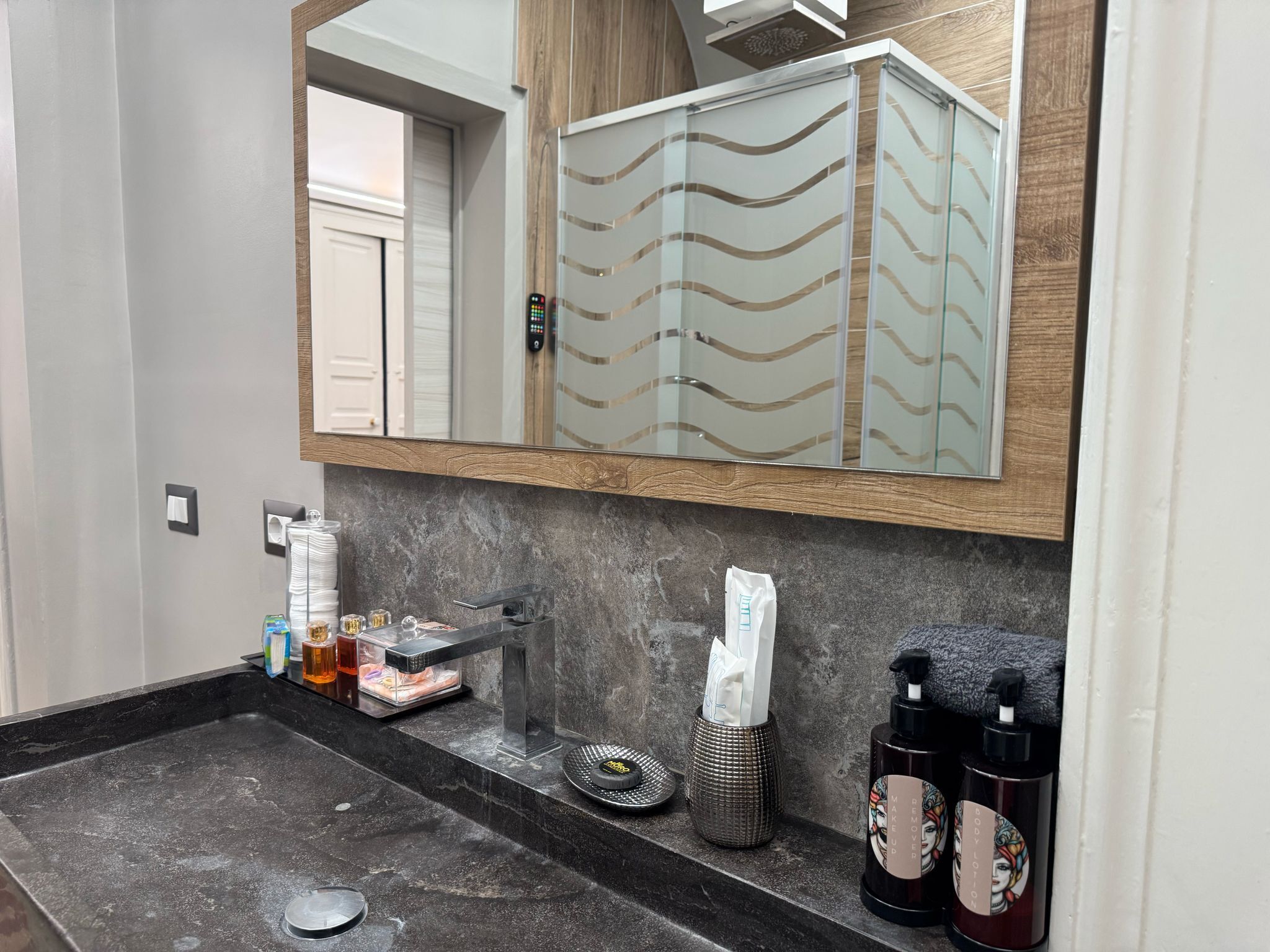 A modern bathroom with a large mirror, a dark marble sink, and various toiletries.