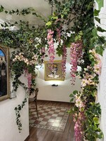 Una habitación con piso a cuadros, un cuadro enmarcado en la pared y plantas colgantes con flores rosadas.