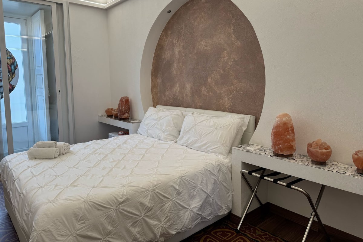 Ein Schlafzimmer mit einem Bett, einem Nachttisch, einem Wandheizkörper und einer Tür.