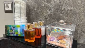 Ein Badezimmer-Waschtisch mit Pflegeprodukten, darunter eine Packung Fazzalotto, mehrere Flaschen Shampoo und Conditioner sowie ein durchsichtiges Gefäß mit Haarschmuckstücken.