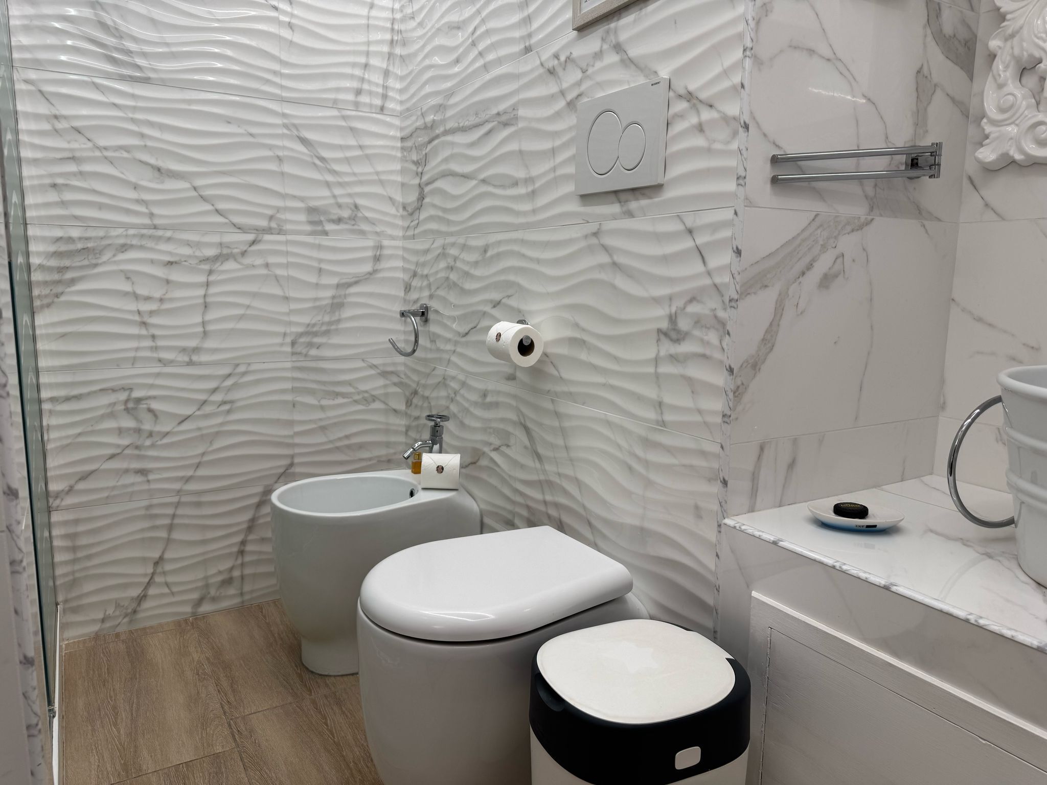 A bathroom with a marble wall, a toilet, a bidet, a sink, and a mirror.