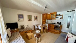 Un ambiente compatto con divano, un piccolo tavolo da pranzo, angolo cottura e televisore.
