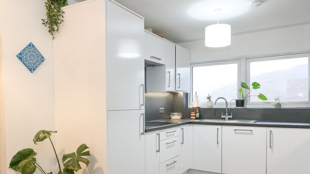 A modern kitchen with white cabinets, a stainless steel sink, and a window with a view of the mountains. - 22 Moray Place (Fort William)