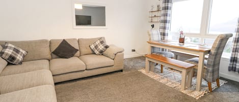 A living room with a sofa, a dining table, and a window with curtains.