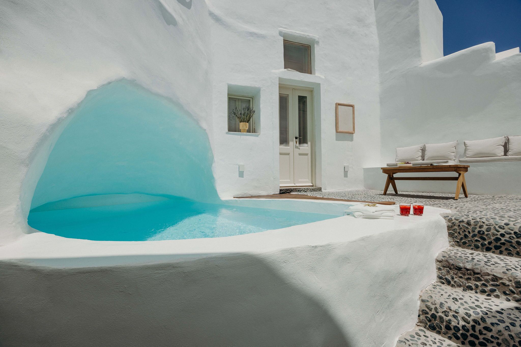 A white-walled building with a blue-tinted pool, a wooden bench, and a door.