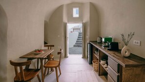 Een smalle gang die uitkomt bij een trap, met aan de ene kant een houten eettafel en stoelen, en aan de andere kant een kitchenette.
