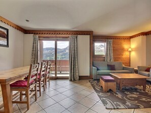 Una sala de estar con una mesa y sillas de madera, un sofá y una mesa de centro. Se ve una vista de montañas a través de las ventanas.