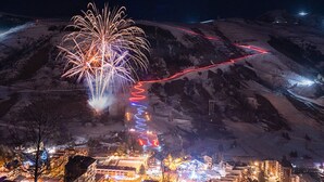 A town with a prominent mountain in the background, a lit pathway, and a large firework display.