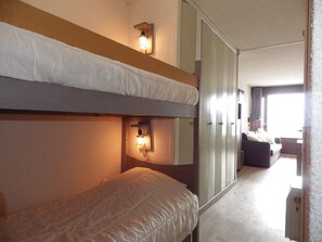 Una habitación de hotel con literas, un armario, un sofá y una lámpara de noche.