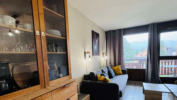 A cozy living room with a wooden cabinet, a sofa with cushions, a coffee maker, and a view of the outdoors.