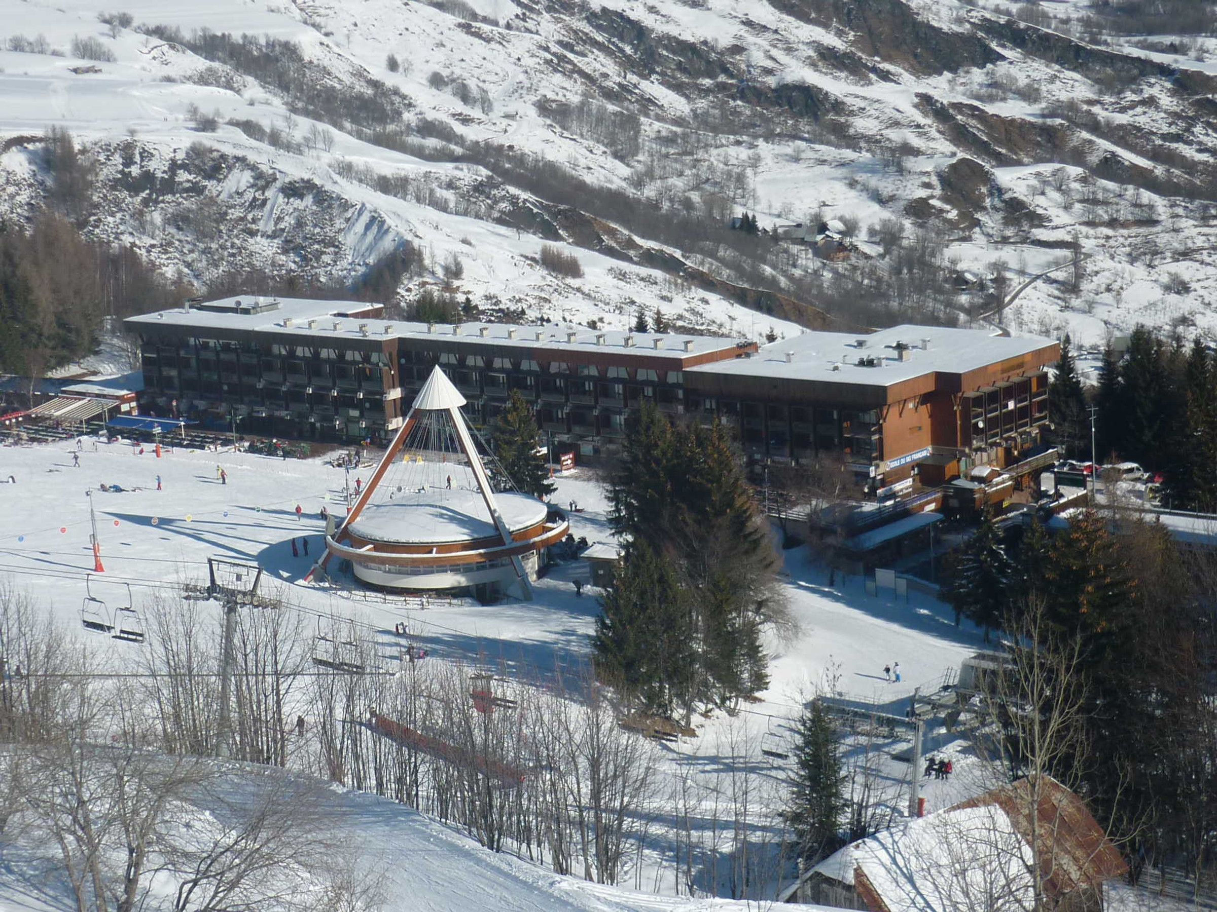 A ski resort with a large building, a ski lift, and a snow-covered mountain in the background.