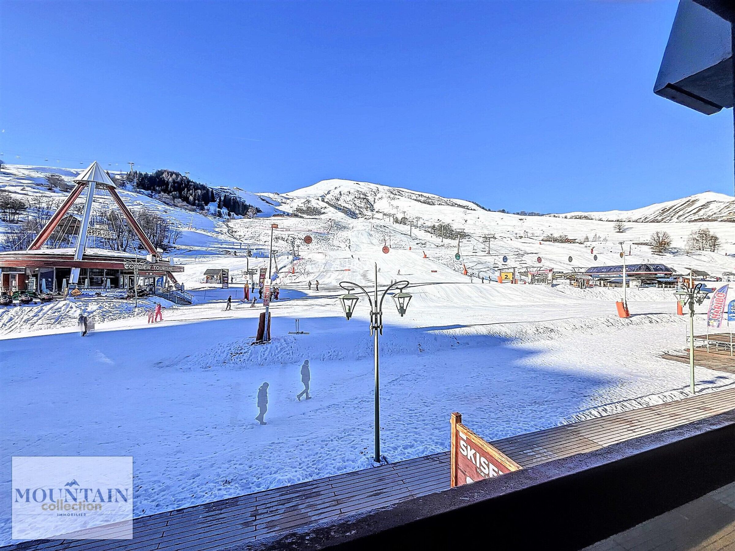 Une station de ski dotée d’un télésiège, avec une vue sur les montagnes en toile de fond et un bâtiment portant l’inscription « Mountain Collection ».