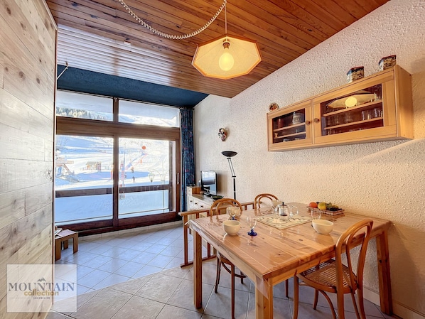A wooden dining area with a table set for four, a large window with a view of a snowy landscape, and a wooden cabinet above the table.