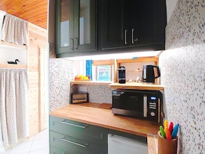 A kitchen with wooden cabinets, a microwave, a coffee maker, and a fruit basket on the counter.