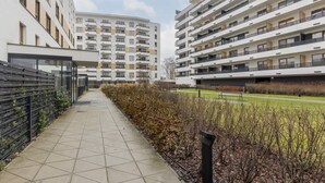 Un immeuble d’appartements moderne, doté de plusieurs étages, d’une galerie couverte et d’un espace paysager agrémenté d’arbustes et d’un sentier.