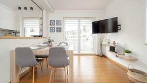 A modern kitchen with a dining area, a flat-screen TV, and a large window.