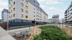 A modern multi-story residential building with balconies, a landscaped garden area, and a pedestrian pathway.