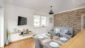 A modern living room with a dining area, a flat-screen TV mounted on the wall, a sofa, and a wooden floor.