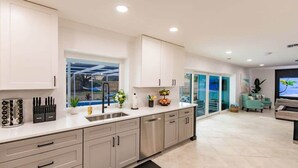 Une cuisine moderne dotée d’une grande fenêtre, d’appareils électroménagers en acier inoxydable et d’un canapé turquoise dans le salon attenant.