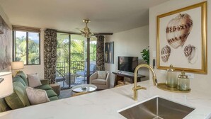 Eine moderne Küche mit Marmorarbeitsplatte, einem goldenen Wasserhahn und einem großen Fenster mit Blick auf einen tropischen Garten.