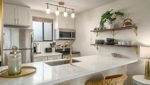Eine moderne Küche mit weißen Schränken, einer großen Insel mit goldenem Wasserhahn und einer hängenden Leuchte.