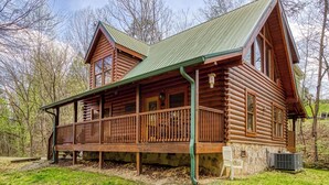 Une cabane en rondins avec une véranda, une cheminée et des fondations en pierre.